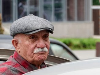 Älterer Mann mit Mütze steigt gerade in sein Auto ein