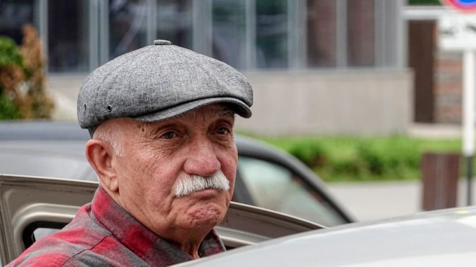 Älterer Mann mit Mütze steigt gerade in sein Auto ein