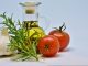 Gemüse, daneben eine Flasche hochwertiges Olivenöl, Tomaten und frische Kräuter auf einem Tisch.