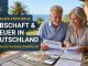 Ein sympathisches, älteres Ehepaar (ca. 65–75 Jahre) sitzt entspannt an einem Holztisch auf einer sonnigen Finca-Terrasse/ Erbschaftssteuer Deutschland sparen